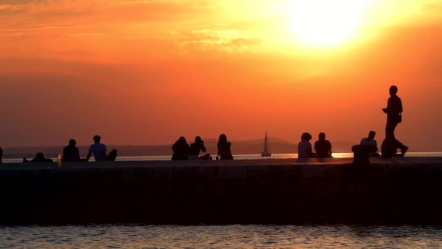 Silhouette slow motion of tourist are watching the sunset with boats and mountains in the background, on the coast of Zadar, Croatia.