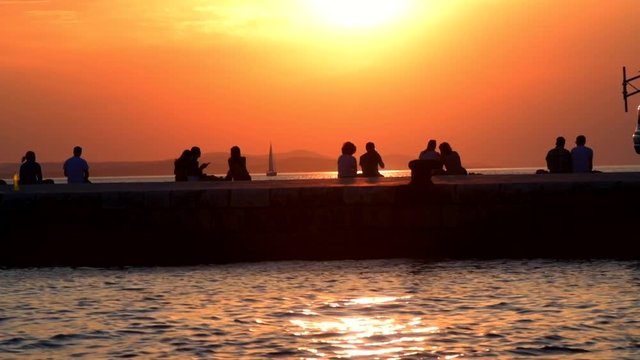 Silhouette slow motion of tourist are watching the sunset with boats and mountains in the background, on the coast of Zadar, Croatia.