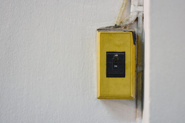 A yellow light switch with a black button is mounted on a white wall.
