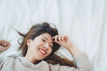 Fototapeta premium Portrait beautiful young Asian woman on bed at home in the morning. Cheerful Asian woman wearing a comfortable sweater and smiling on her bed. Relaxing room. lifestyle asia woman at home concept.
