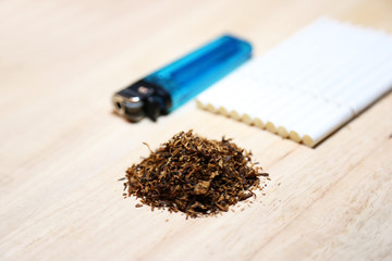 Closeup dry tobacco leaves with cigarette and lighter isolated in wood plate.