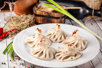 Traditional Georgian and Armenian cuisine. Georgian khinkali with meat on a white plate, on a wooden table in a restaurant. Wine on the table. Copy space, selective focus