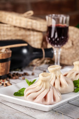 Traditional Georgian and Armenian cuisine. Georgian khinkali with a cherry on a white plate, on a wooden table in a restaurant. Wine on the table. Copy space, selective focus