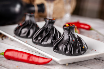Traditional Georgian and Armenian cuisine. Trend, Georgian black khinkali with meat and suluguni cheese, on a wooden table in a restaurant. Wine on the table. Copy space, selective focus