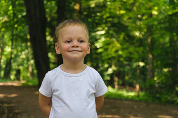 Portrait of a boy in a white T-shirt against a background of green leaves