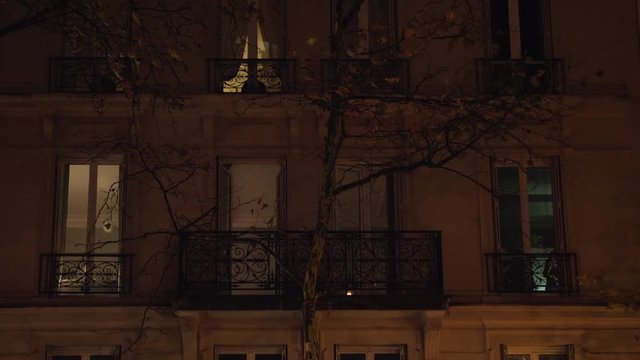 PARIS, FRANCE - SEPTEMBER 29, 2017: Night view of the house and bare autumn tree in dim light of street lantern, people can be seen in the windows