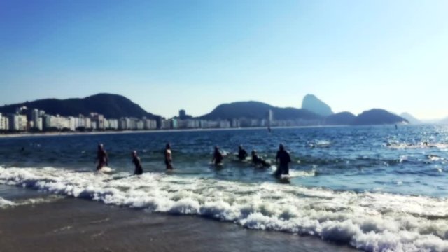Group of swimmers coming ashore in slow motion on Copacabana Beach against a dramatic skyline view of Rio de Janeiro, Brazil