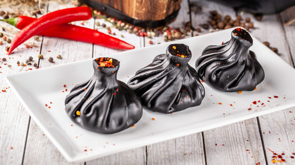 Traditional Georgian and Armenian cuisine. Trend, Georgian black khinkali with meat and suluguni cheese, on a wooden table in a restaurant. Wine on the table. Copy space, selective focus