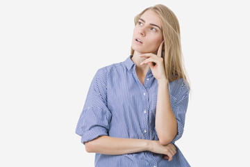 Portrait of young blonde european girl wearing blue striped shirt thinking about something over white background