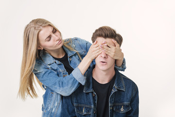 Girlfriend covering the eyes of her boyfriend for a surprise. Studio shot over white background