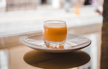 Healthy shot of functional organic fruit, vegetable and spice in a small glass on a white saucer in the bright window of a health bar