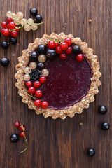 Raw vegan pie made of nuts and berry jam decorated with black, red and white currants on wooden background copyspace