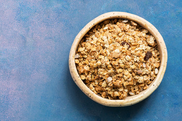 Organic homemade granola grain with oats, nuts and raisins in a clay bowl on a blue background. The view from the top, flat lay.