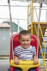 Baby 2 years riding on a swing. Happy child on the playground. ertical photo.