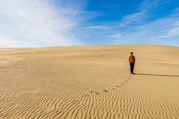 Lonely man stands in desert with footprints on the sand in sunny day