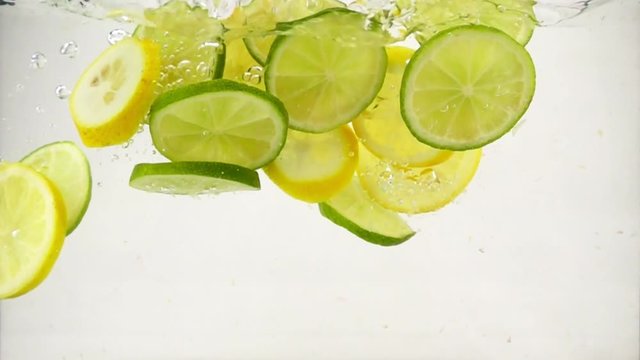 Slices of lime and lemon fall into a water with splashes and bubbles, slow motion close-up
