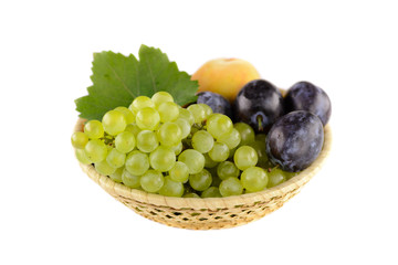 A bowl of tasty, ripe summer fruits with white background. In the bowl peach, plum and white grapes.