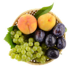 A bowl of tasty, ripe summer fruits with white background. In the bowl peach, plum and white grapes. Top view