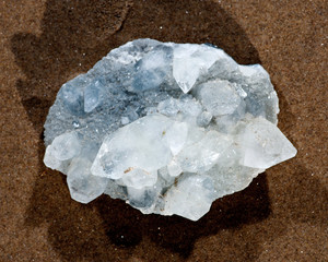 Lustrous Apophyllite crystal cluster from India on wet sand near water on the beach at sunrise. Phyllosilicates. 