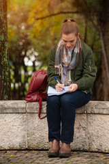 Obraz premium Portrait of a cute young female student studying outdoors in a summer park with notebook