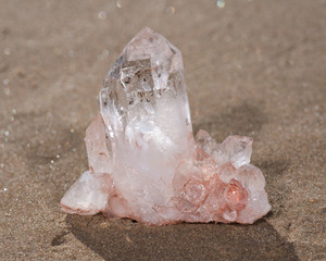 Himalayan clear quartz cluster with hematite inclusions on wet sand on the beach at sunrise.