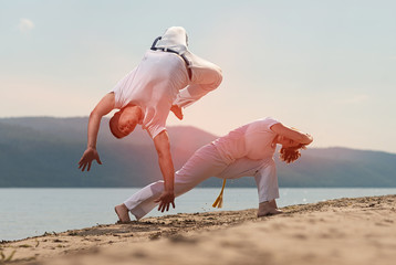 Men train capoeira on the beach - concept about people, lifestyle and sport.
