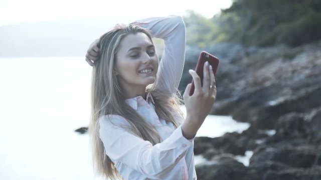 Pretty girl takes selfies on the beat at sunny sea. 4K