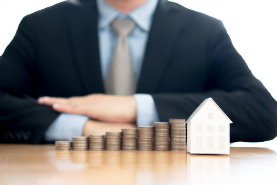 Stack of increasing coins and house model with businessman crossing his arms