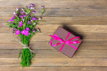 bouquet of carnations and brown box with a gift on a wooden background, flat lay top view