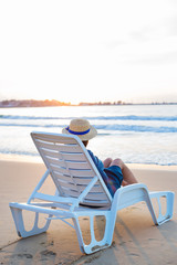 Beautiful girl in a hat sits on a deckchair meeting the dawn.