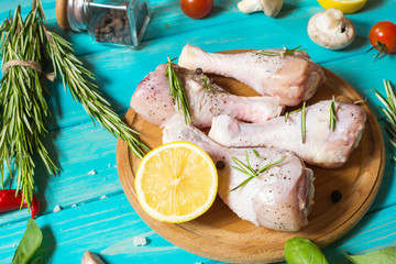 Raw uncooked chicken legs, drumsticks on blue wood background, meat with ingredients for cooking.