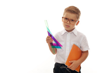 Serious little boy with blond hair in glasses looks at the camera and shows his office supplies for school. Place for text