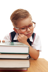 Smart little boy wearing eyeglasses an elementary school student sitting at school desk with books on white background