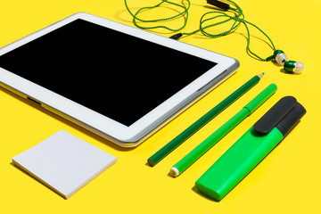 set of business or education accessories. green pencils, headphones, paper stickers, markers and tablet pc lying on a yellow background. concept of the office gadgets and stationary