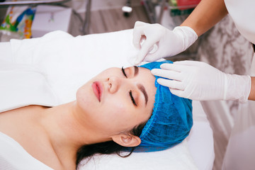 Beautiful young Asian woman getting her face cleansed by beautician at cosmetology beauty clinic.