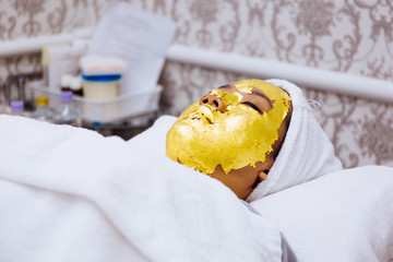 Young woman getting 24 karat gold facial treatment at the beauty clinic. The treatment of using real gold for youthful skin.