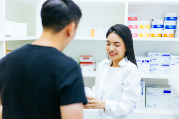 Fototapeta premium Asian female pharmacist doctor in professional gown explaining and giving advice with male client in drugstore shop.