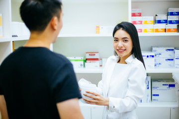 Obraz premium Asian female pharmacist doctor in professional gown explaining and giving advice with male client in drugstore shop.