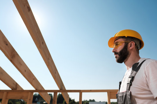 The man is a builder on the roof of a wooden frame house.