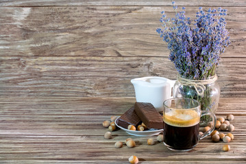 A photo of a fragrant black coffee in a glass mug next to chocolate cakes, hazelnuts, a white jug...
