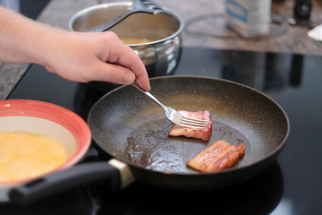 Preparation of scrambled eggs and bacon for breakfast on an electric stove in the kitchen