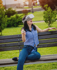 A beautiful young girl plays a game wearing virtual reality glasses on the street.