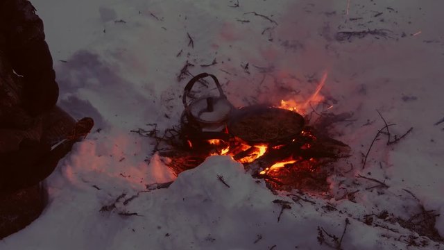Cree man warming food and tea in winter over fire in the snow, northern Quebec