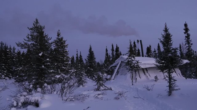 Cree camp tent in winter at dusk, with chimney smoke and moon, snow and forest