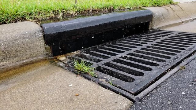 Water drips and drains into a storm drain on the side of the street