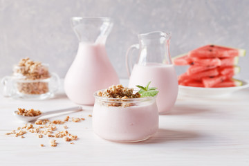 Fruit yogurt, smoothies in a glass jug, granola and sliced watermelon on  white wooden background. Close-up, selective focus, shallow depth of field.
