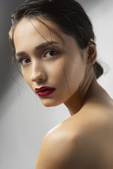 Naklejka premium Beautiful brunette girl fashion model with naked shoulders and wet hair on a gray background. Nude make-up, red lips. Healthy clean skin