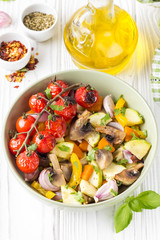 Baked vegetables with mushrooms in a bowl. Zucchini, cherry tomatoes on a branch, red onions, bell peppers and garlic. Delicious garnish, vegetarian food, healthy diet