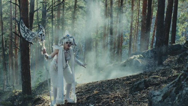 Mythological character satyr is strolling in a woodland in sunny day. It is holding axe and looking around, artistic shooting