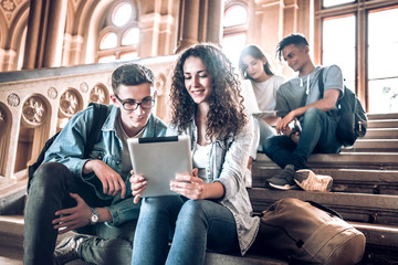 College life.Group of students using a tablet while sitting on stairs in university.